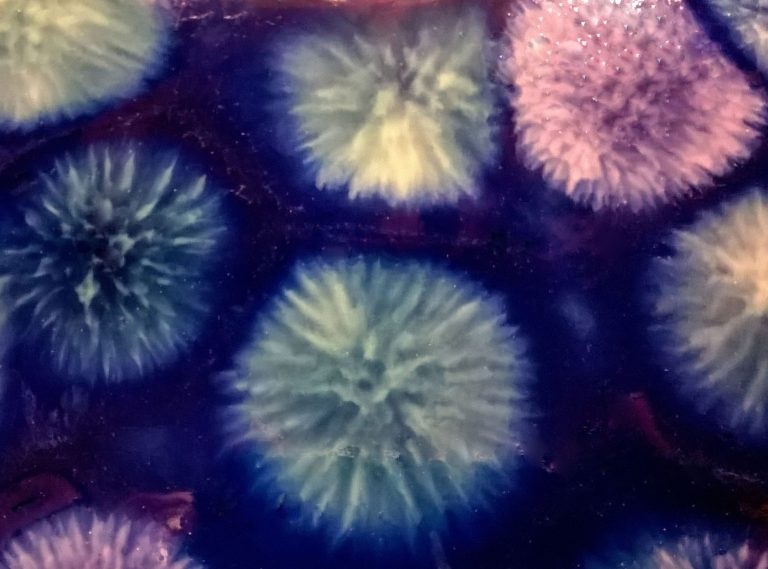 Detail image of glaze that looks like fireworks in colors of dark blue, light green and violet.