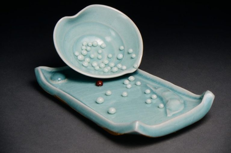 Image of a cup and saucer with celadon glaze and several Kiln Jewels spilling out of the cup on to the saucer.