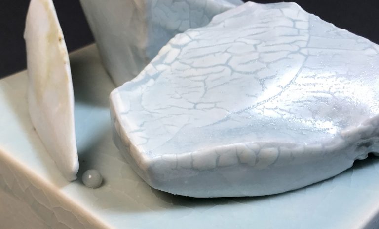 Detail image of porcelain glaciers in soft blue, white, and textual glazes that sit on a white pedestal.