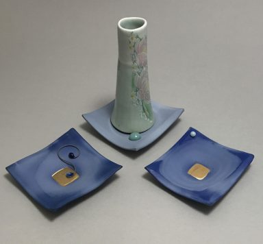 Three sculptural saucers and one cup with wire handle. Non-functional sculpture in shades of blue with flower decals and gold enamel..