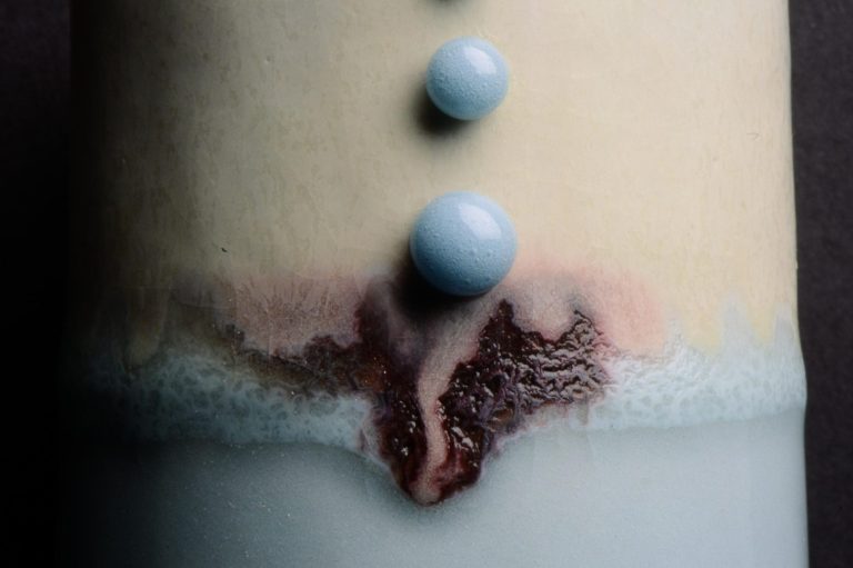 Close up of a vessel with red, white and blue glaze and two blue Kiln Jewels 